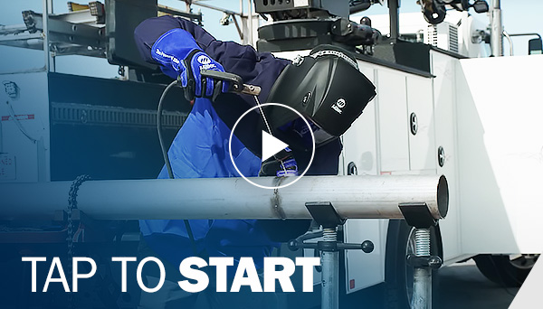 Operator stick welds a pipe while standing next to a work truck. Image has a play button and words TAP TO START